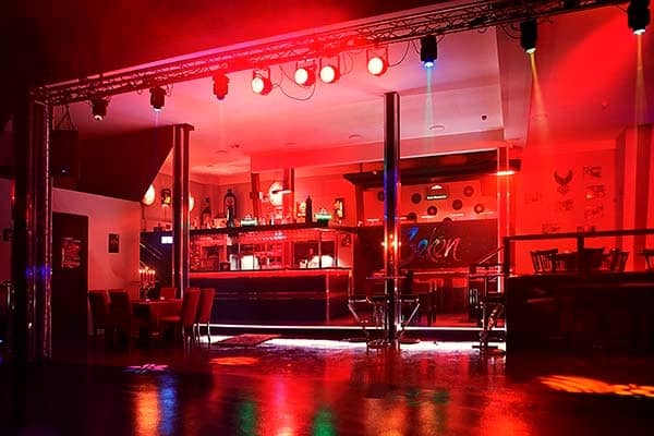 Blick über die Tanzfläche zur Bar: warm und rot ausgeleuchteter Saal mit Lichttraverse und Scheinwerfern