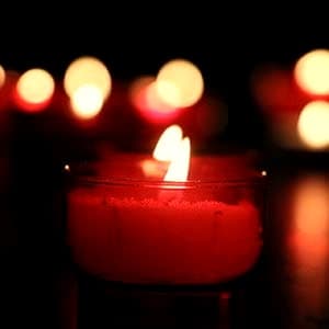 Brennende Kerze in rotem Glas vor warmem Lichterhintergrund