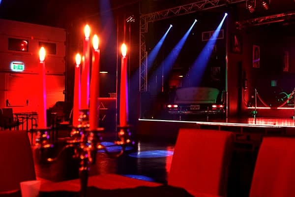 Saal im Dreibeken mit roten Kerzenleuchtern und roten Sitzbänken, im Hintergrund die beleuchtete Bühne