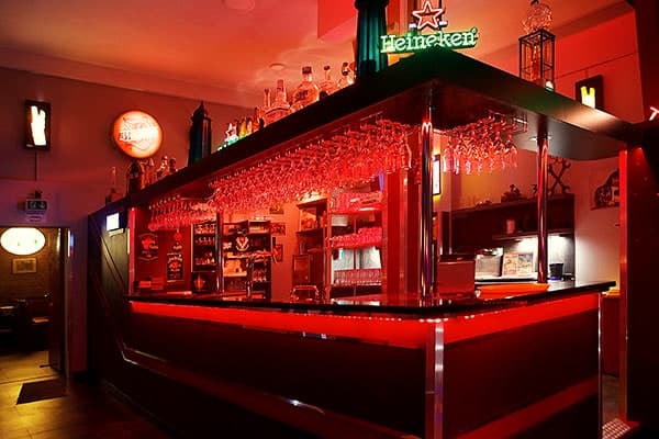 Klassische Bar im Dreibeken mit rot beleuchtetem Tresen, Gläsern und gut bestücktem Flaschenregal